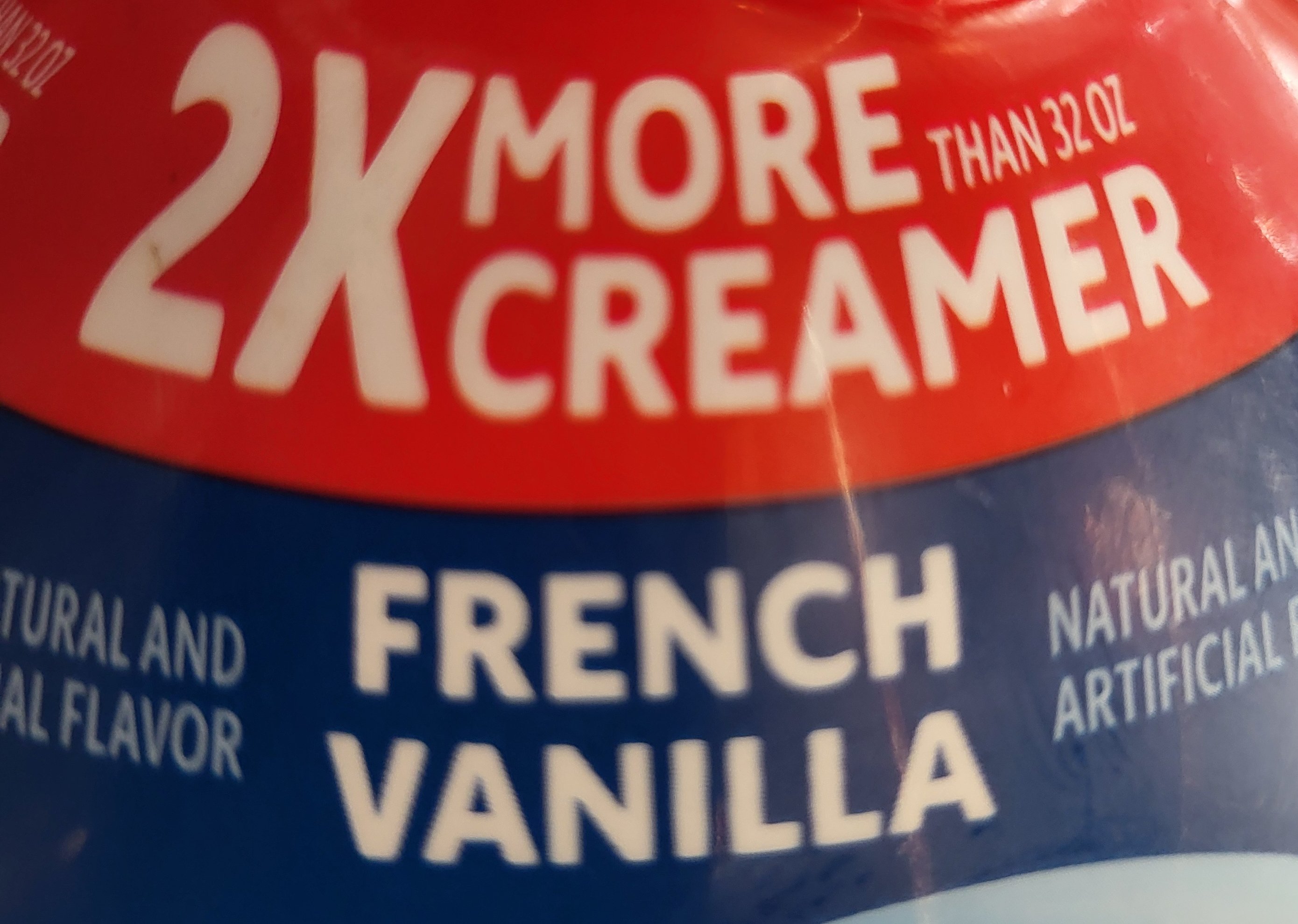 A close-up photo of a 64 ounce bottle of coffee creamer. In large, bold text on a bright red banner, it says '2x more creamer,' but in fine print clarifies 'than 32 ounce.'